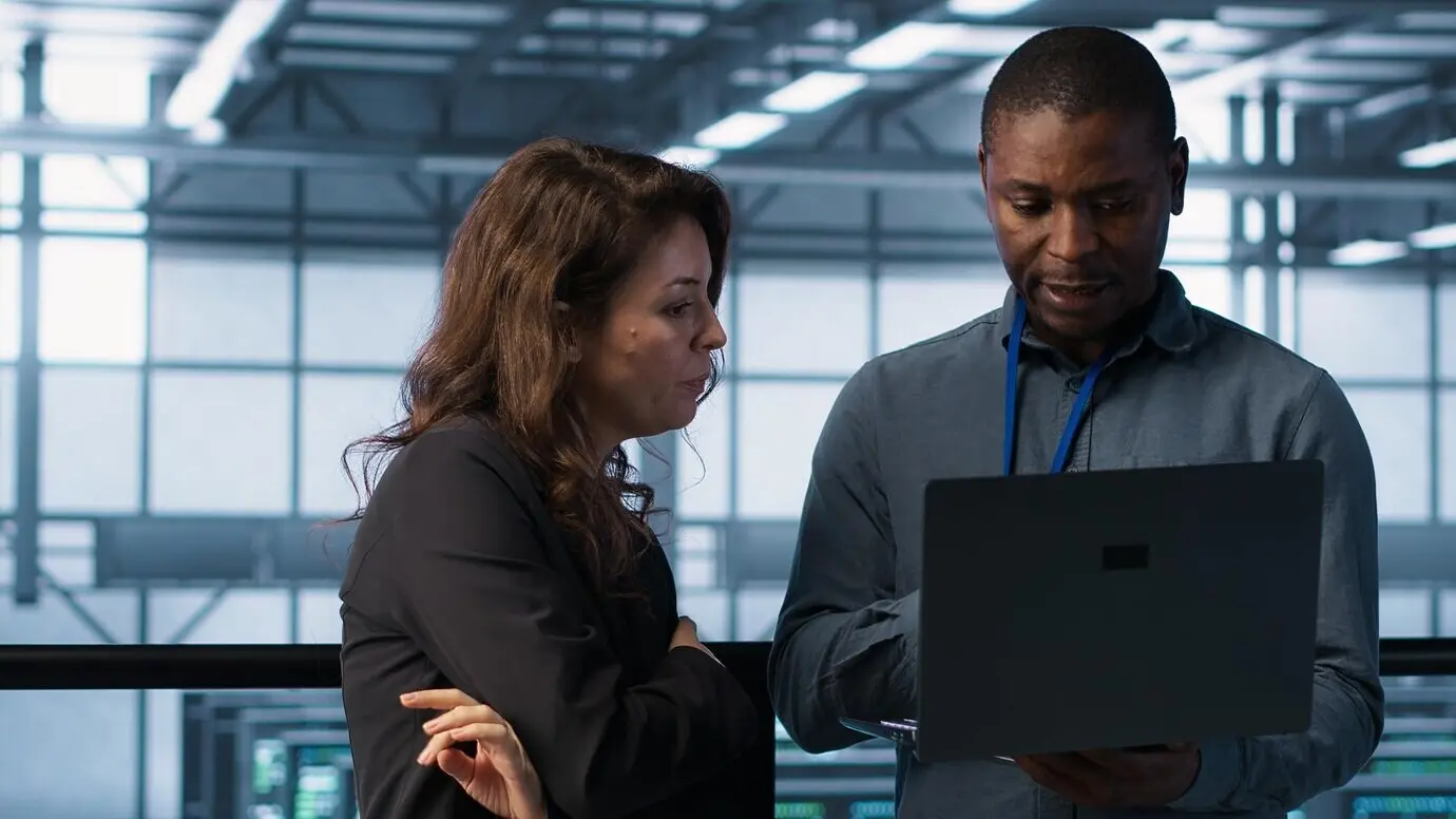 Разработчики в рабочем пространстве дата‑центра программируют на ноутбуке и анализируют метрики.